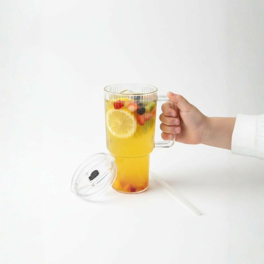 Glass tumbler with handle beside fresh juice and fruit