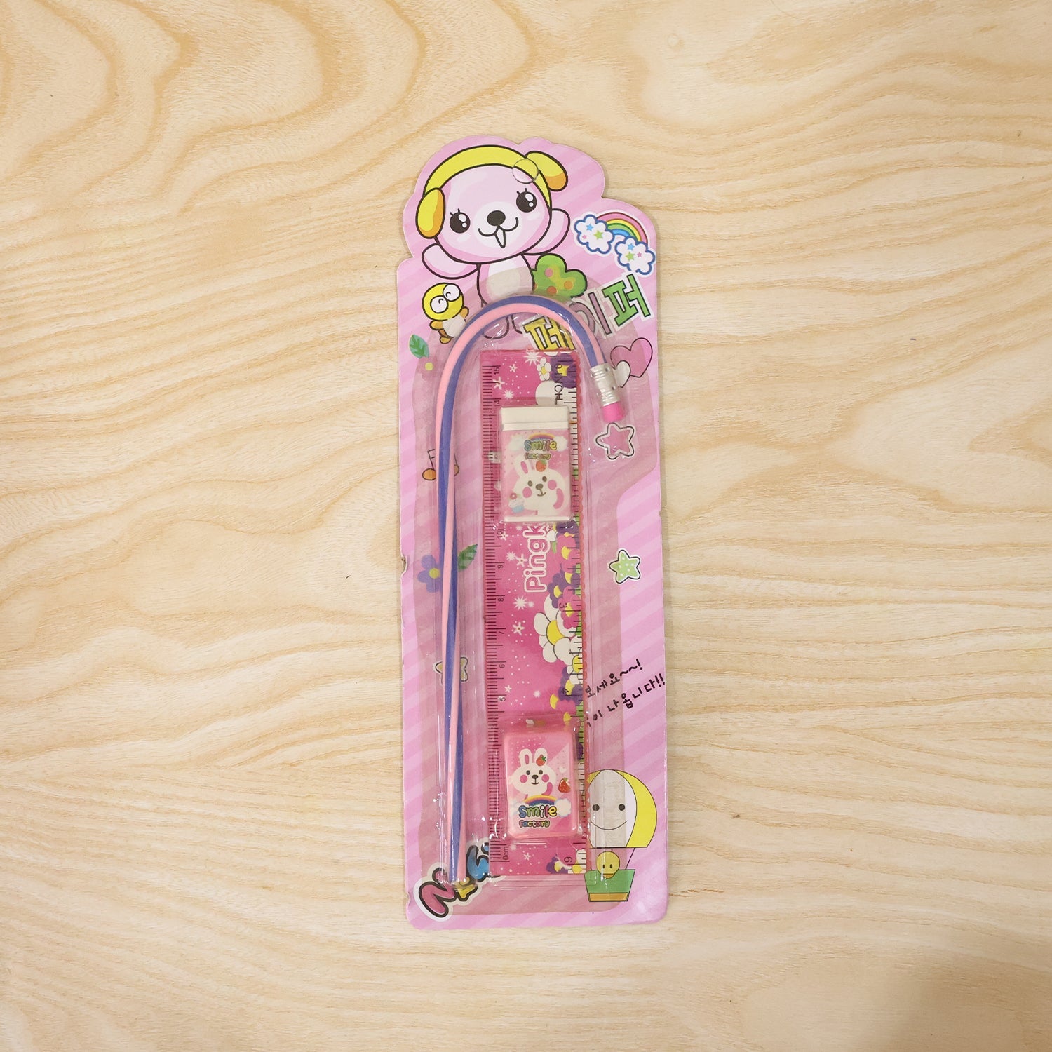 Pink stationery set displayed in use, showing ruler, pencil, eraser, and sharpener.